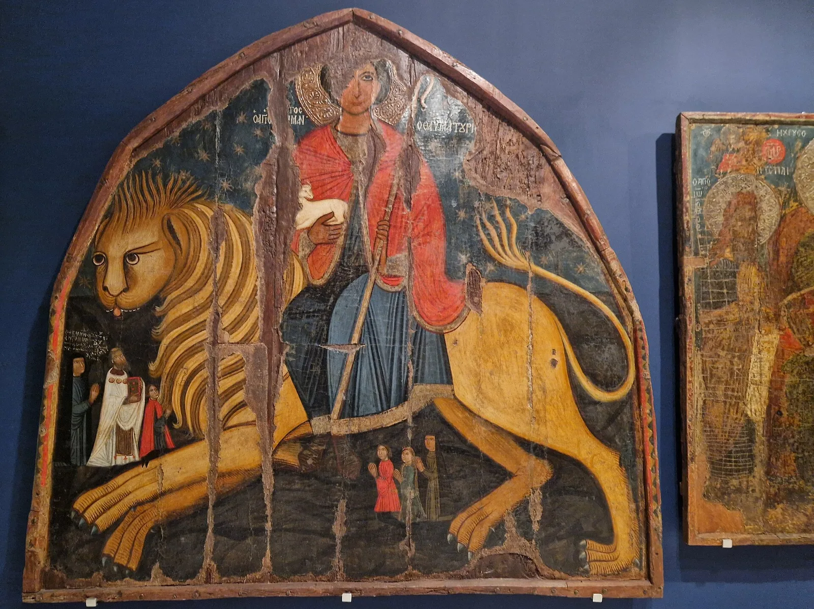 Arched icon of St Mamas riding a large lion, displayed in a museum gallery